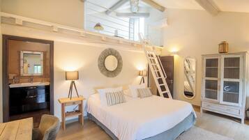 Un dormitorio con techo estilo loft, una cama con ropa de cama blanca, una mesita de noche, un espejo, un armario y un pequeño escritorio con silla.