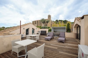 An outdoor patio with wicker furniture, a grill, and a view of a historic building in the background. - Boutique Hôtel La Villa Montesquieu (Laudun-l'Ardoise)