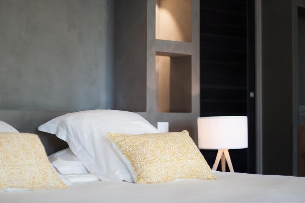 A hotel room with a bed, pillows, a bedside lamp, and a view through a window.