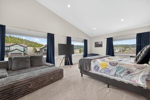 A bedroom with a bed, a sofa, a TV, and a large window with a view of houses and trees. - Magnificent mt home, private HT, mt views, game room and more! (Tabernash)
