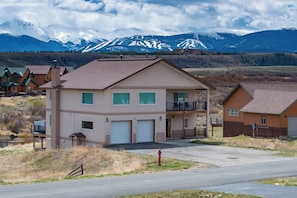A two-story building with a garage, a balcony, and a view of snow-capped mountains. - Magnificent mt home, private HT, mt views, game room and more! (Tabernash)