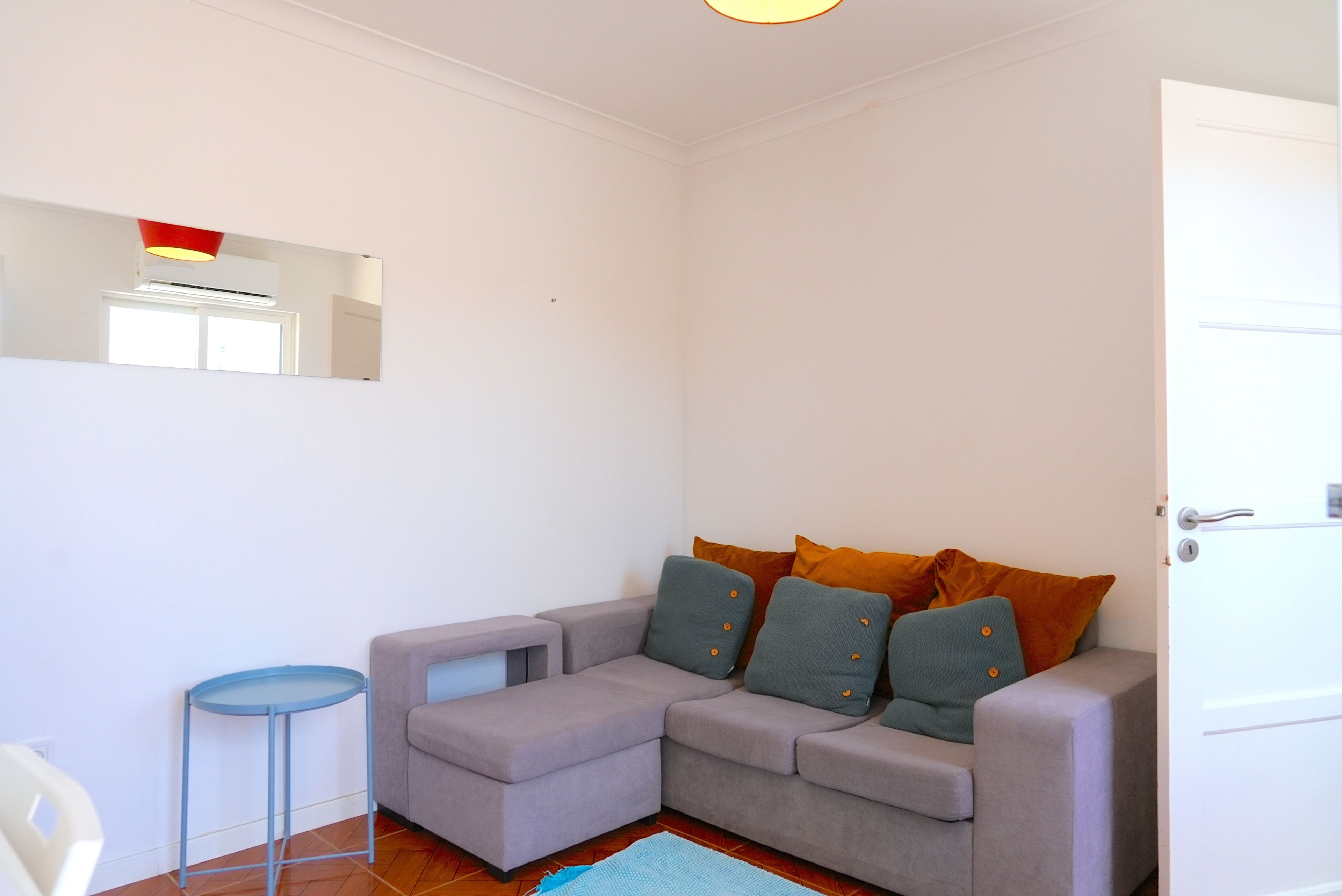 Um quarto com um sofá cinzento, uma pequena mesa azul e uma porta.