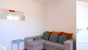 Um quarto com um sofá cinzento, uma pequena mesa azul e uma porta.