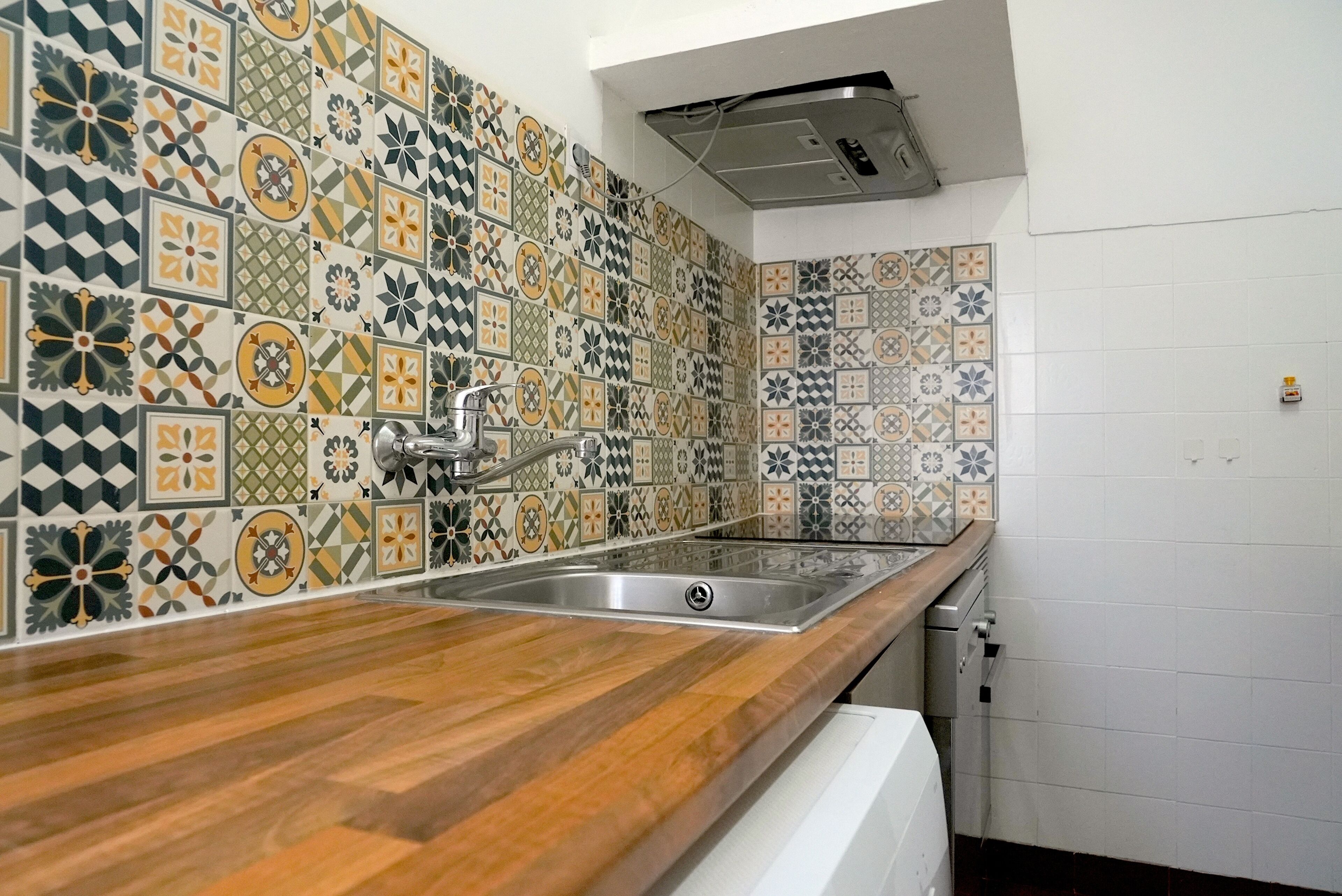 Uma cozinha com bancada de madeira, pia de aço inoxidável e painel de fundo com padrão.
