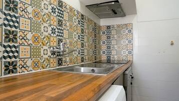 Uma cozinha com bancada de madeira, pia de aço inoxidável e painel de fundo com padrão.