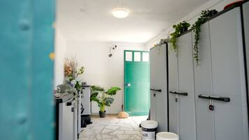 Um corredor com armários, uma porta verde, plantas em vasos e piso de pedra.