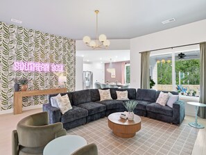 Un salon moderne avec un canapé d’angle, une table basse ronde et un néon mural.