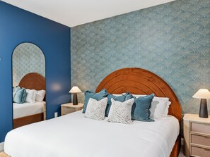 Ein Schlafzimmer mit einem großen Bett, zwei Nachttischen, einem Beistelltisch, einem Spiegel und einer Wand mit Muster.