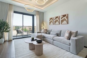 Ein modernes Wohnzimmer mit einer Eckcouch, zwei runden Couchtischen, einem großen Fenster mit Vorhängen und abstrakter Wandkunst.