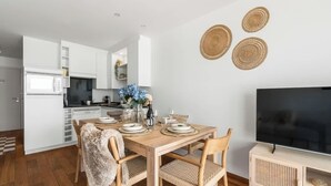 Una cocina moderna con armarios blancos, una mesa de comedor dispuesta con platos y vasos, y un televisor de pantalla plana sobre un atril de madera.