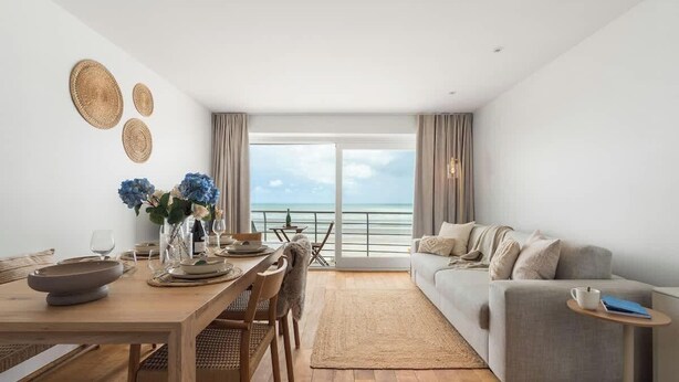 Una sala de estar moderna con comedor, un sofá y vista al mar.