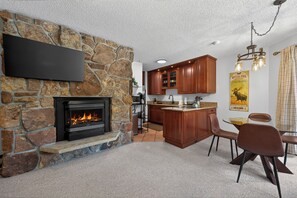 A stone fireplace with a TV above it, wooden cabinets, and a kitchen area with a bar.