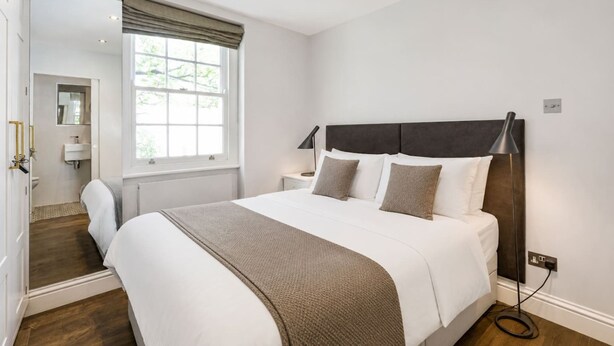 Un dormitorio con una cama grande, una ventana con cortinas, una lámpara de noche y un espejo en la pared.