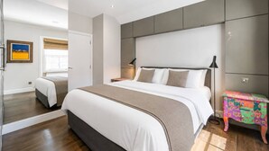 Un dormitorio moderno con una cama grande, mesitas de noche, una mesita auxiliar y una ventana con vistas.