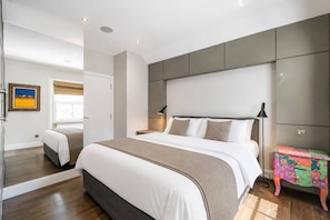 Ein modernes Schlafzimmer mit einem großen Bett, Nachttischen, einem Beistelltisch, einem farbenfrohen Nebentisch und einem Fenster mit Blick.