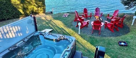 A hot tub with a view of a lake and red Adirondack chairs.