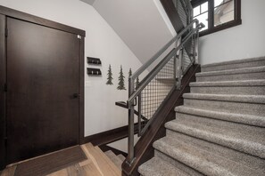 A staircase with wooden steps and a metal railing, leading to a landing with a dark wooden door and a small wall-mounted light fixture. - 200 Quill Court 4 bedroom home, private HT, 2 living spaces, EV car charger (Fraser)