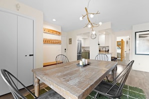 A dining area with a wooden table, chairs, a chandelier, and a kitchen in the background. - The Colony Unit #102 Ground floor, renovated, private patio, near outdoor trails (Fraser)