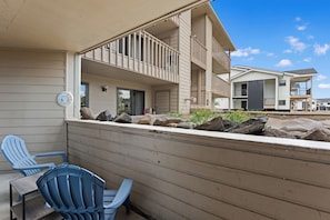 A residential building with a balcony, a small garden area with rocks and plants, and two blue Adirondack chairs. - The Colony Unit #102 Ground floor, renovated, private patio, near outdoor trails (Fraser)