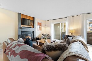 A living room with a fireplace, leather sofa, and a view through a glass door. - The Colony Unit #102 Ground floor, renovated, private patio, near outdoor trails (Fraser)