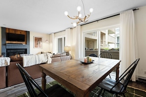 A dining area with a wooden table, black chairs, a chandelier, and a fireplace. - Ground floor, renovated, private patio, near outdoor trails (Fraser)