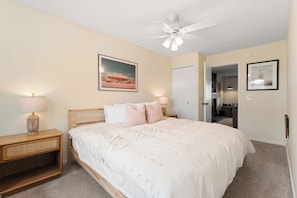 A bedroom with a bed, nightstands, a ceiling fan, and a door leading to another room. - Ground floor, renovated, private patio, near outdoor trails (Fraser)
