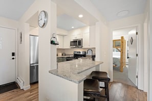 A modern kitchen with a central island, stainless steel appliances, and a wooden bench. - The Colony Unit #102 Ground floor, renovated, private patio, near outdoor trails (Fraser)