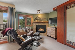 A living room with a fireplace, leather recliner, and a television. - Iron Horse Building D Unit 3074 High end studio, ski-in/ski-out, forest views (Winter Park)