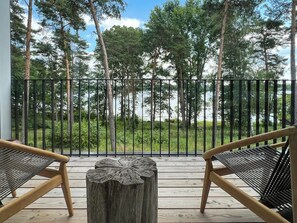 A wooden deck with two chairs and a central wooden table, overlooking a forested area.