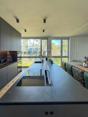 A modern kitchen with a central island, large windows, and a view of trees and buildings outside.
