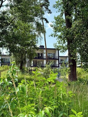 A modern building with balconies, surrounded by lush greenery.