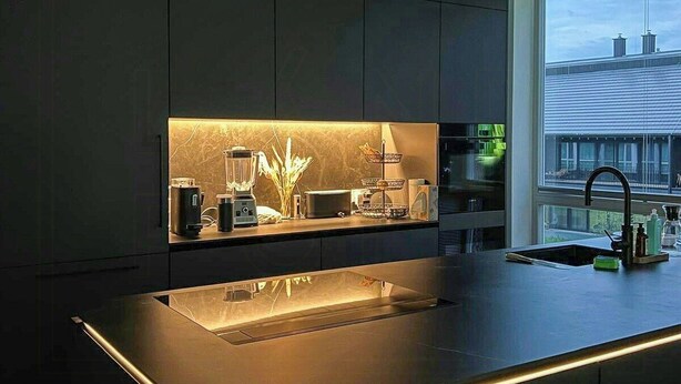Een moderne keuken met een centraal eiland, inbouwapparatuur en een groot raam.