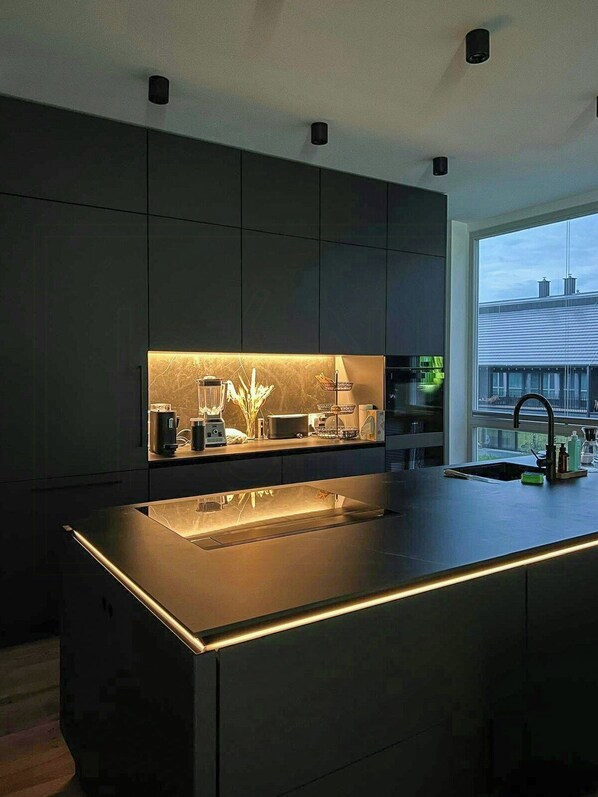 A modern kitchen with a central island, built-in appliances, and a large window.