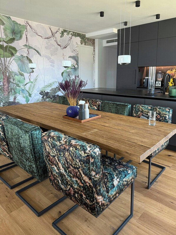 A modern dining area with a wooden table, patterned upholstered chairs, and a wall mural.