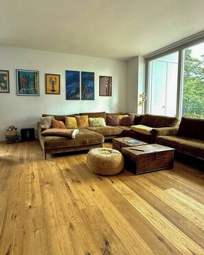 A living room with a brown sofa, ottoman, and coffee table, wooden flooring, and artwork on the wall.