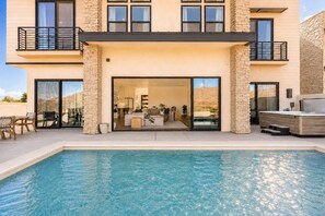Ein modernes, zweistöckiges Haus mit Swimmingpool, Steinaußenwand und Balkon.