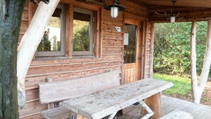 Een rustieke houten blokhut met een overdekte veranda, een bank en een hanglamp.