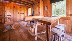Een rustiek houten interieur met houten wanden, een grote houten tafel, banken en een open haard.