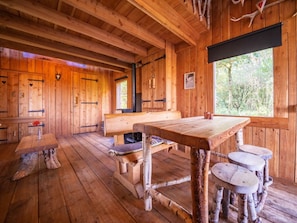 Ein rustikales Blockhaus-Interieur mit Holzwänden, einem großen Holztisch, Bänken und einem Kamin.