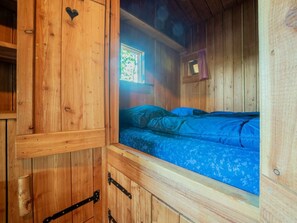 Ein Holzblockhaus im Inneren, mit einem Bett, einem Fenster und einer kleinen Holzkommode.