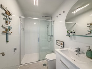 Un baño moderno con ducha de vidrio, inodoro blanco y lavamanos con espejo.