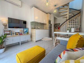 Una sala moderna con televisor de pantalla plana, comedor, escalera y cocina.