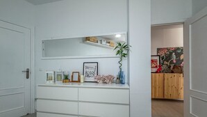Käytävä, jossa on valkoinen ovi, valkoinen seinä, jossa on hylly, ja puinen kaappi, jossa on juliste.