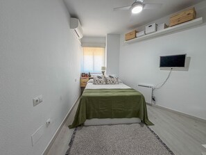 Un dormitorio con cama, televisión, ventilador de techo y ventana con vista.