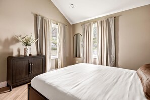 Un dormitorio con cama, cómoda, espejo y cortinas.
