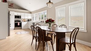 Une cuisine moderne avec des meubles blancs, une table à manger avec des chaises et un luminaire suspendu.