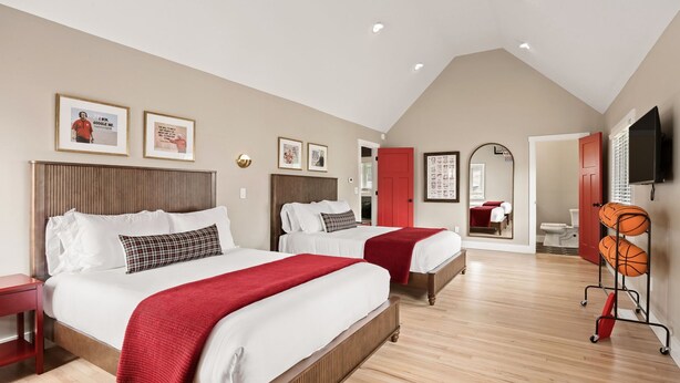 Une chambre d’hôtel avec deux lits, un téléviseur, une porte rouge et un porte-ballon de basket.