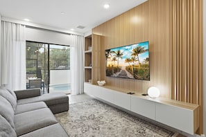 A modern living room with a flat-screen TV mounted on a wooden wall, a grey sofa, and a patterned rug. - Luxury 5BR Villa w/ 4 Private Suites | Heart of Orlando (Orlando)