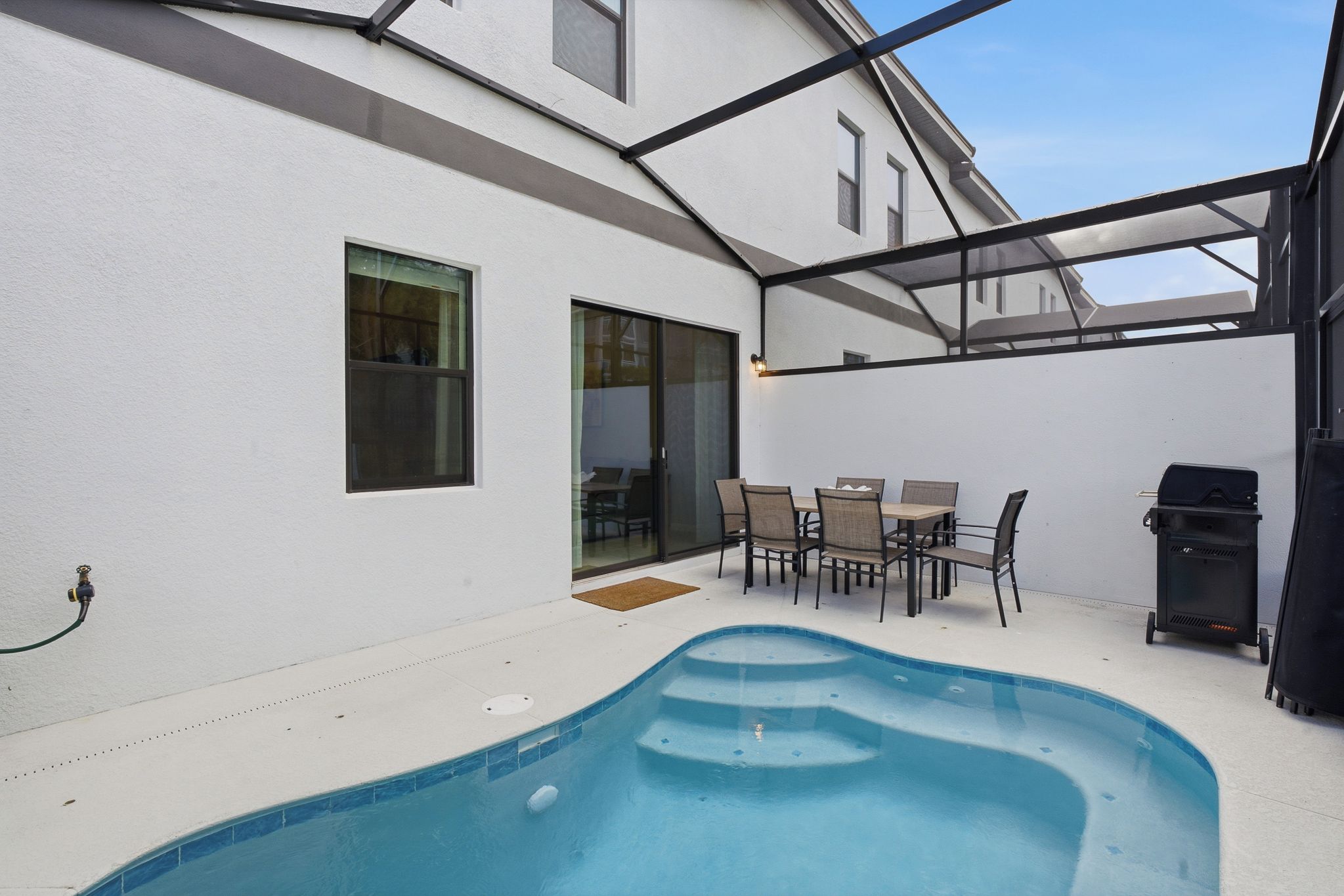 A backyard with a swimming pool, a covered patio area, and a barbecue grill.