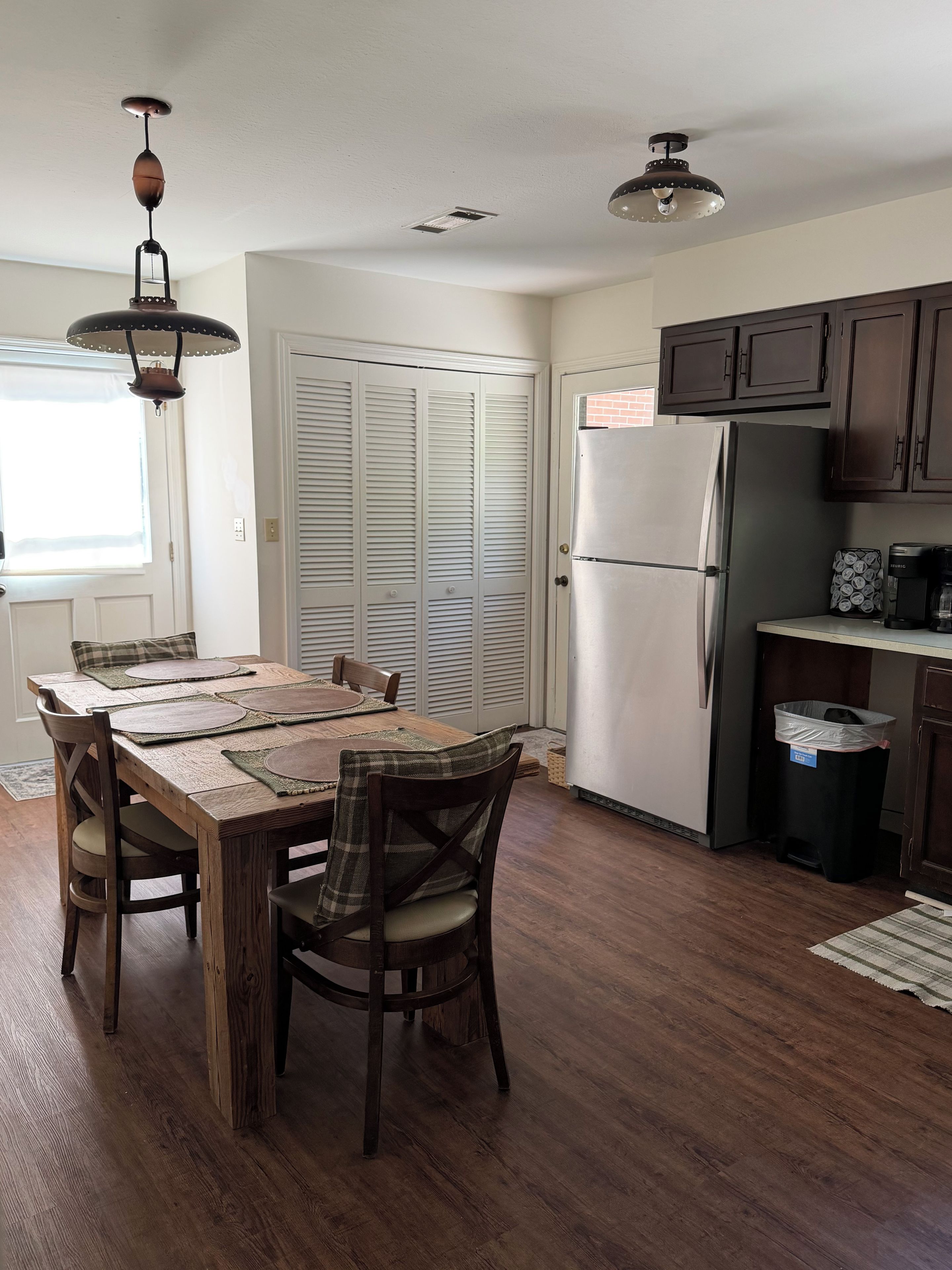 A kitchen with a dining table, chairs, a refrigerator, cabinets, and a ceiling fan.